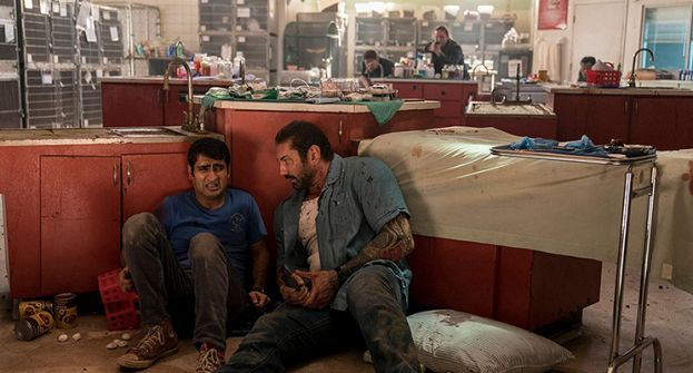 Kumail Nanjiani, as the Uber driver, and Dave Bautista, as the veteran cop, taking cover from the villain in the movie, Stuber.