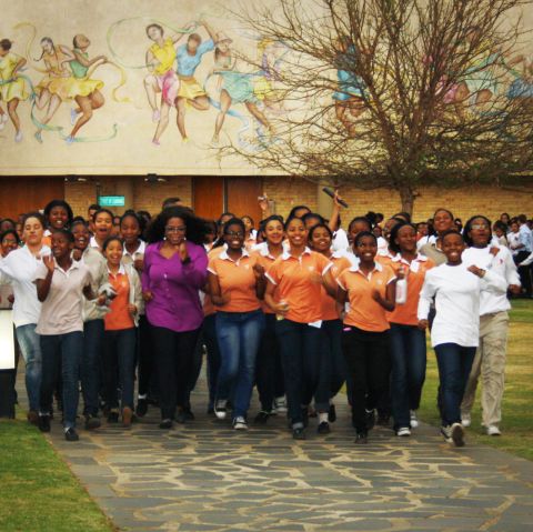 Oprah Winfrey walking briskly with students from the Oprah Winfrey Leadership Academy for Girls in South Africa. They are using Omron pedometers to keep track of their steps, as part of a fittest school challenge